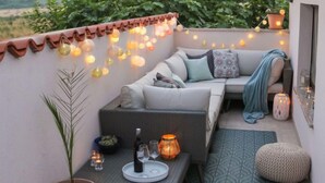 Uma área de estar acolhedora ao ar livre, com um sofá, uma mesa pequena com bebidas e luzes de Natal.