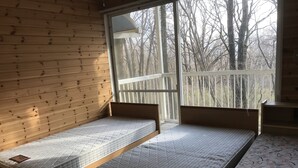 Una cabaña con dos camas de madera y un ventanal grande con vista a un bosque.