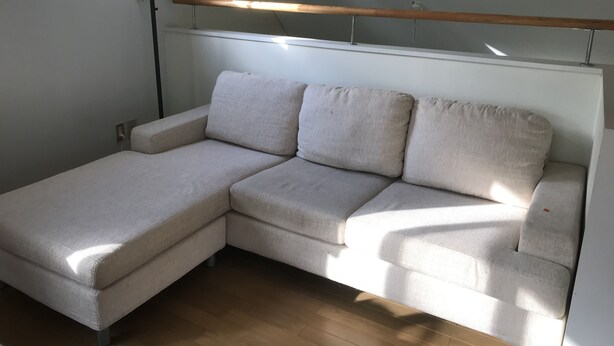 Una habitación con un sofá seccional en forma de L, un lámpara en el techo y un ventanal que deja entrar luz natural.