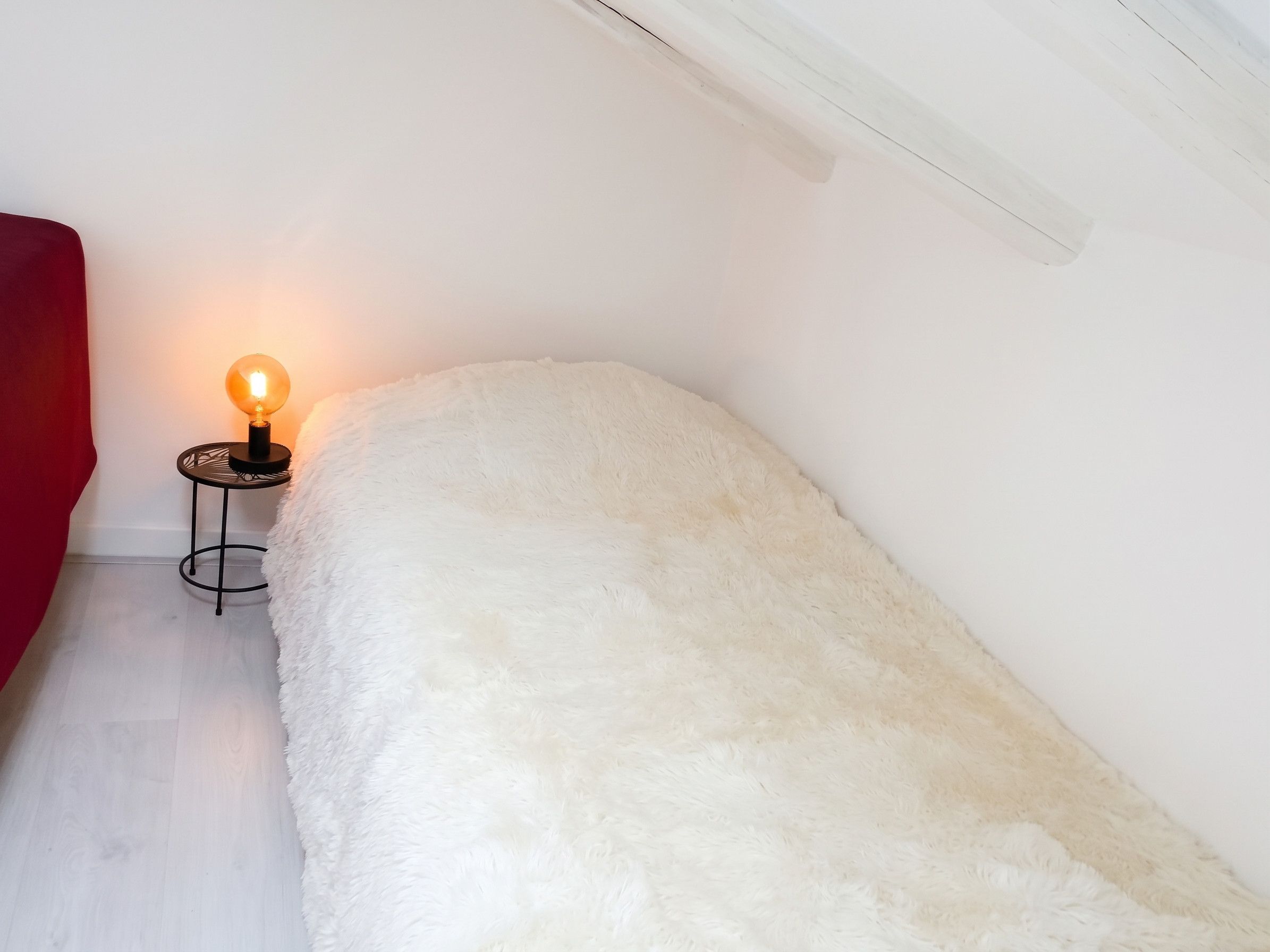 Ein weißes, flauschiges Bett in einem Zimmer mit einem kleinen Tisch und einer Lampe.