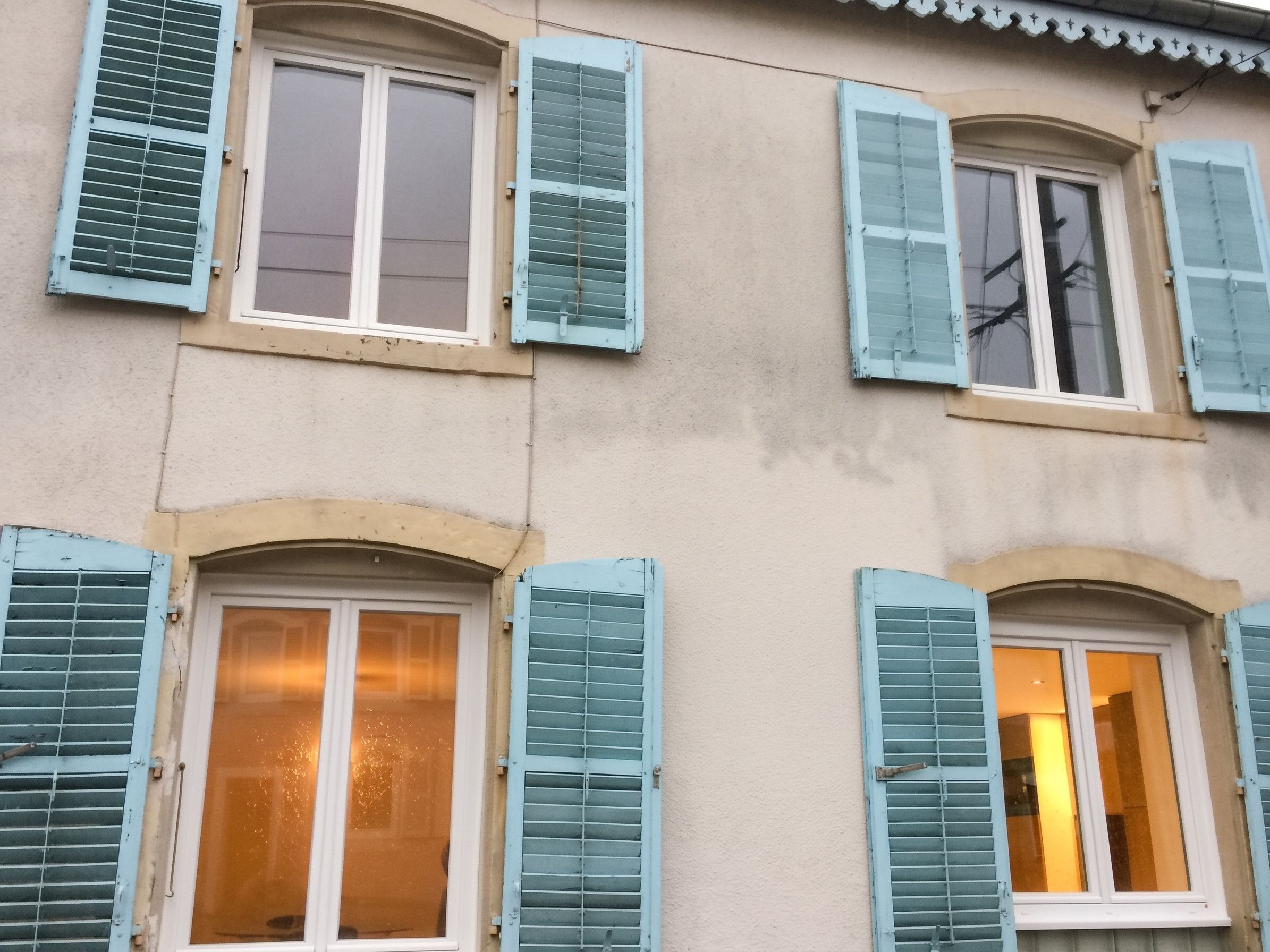 A building facade with multiple windows, some with shutters, and a textured wall.