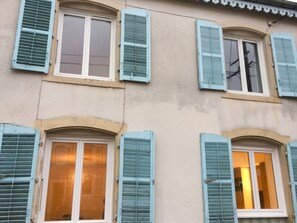 Une façade d’immeuble avec de nombreuses fenêtres, dont certaines sont dotées de volets, et un mur à la texture particulière.