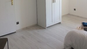 Una habitación con un armario blanco, una cama con edredón blanco y una lámpara colgante.