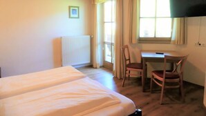 Ein Zimmer mit zwei Betten, einem Schreibtisch, einem Stuhl, einer Heizung und einem fenster mit Vorhängen.
