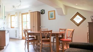 Ein Essbereich mit einem Holztisch und -stühlen, im Hintergrund eine Küche und ein kleines Fenster mit Aussicht.