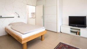 Un dormitorio con cama, televisor, armario y una pequeña cocina.
