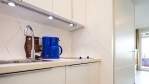 Una cocina moderna con armarios blancos, un salpicadero de mármol, una cafetera azul y un fregadero de acero inoxidable.