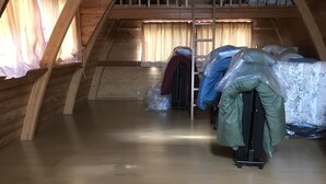Habitación en ático con vigas de madera, una cama tipo litera, un taburete pequeño y una maleta.