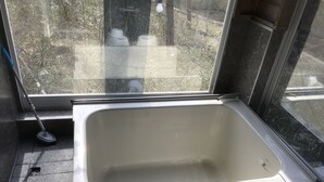 Un baño con un ventanal grande, un lavamanos y una escoba apoyada en la pared.