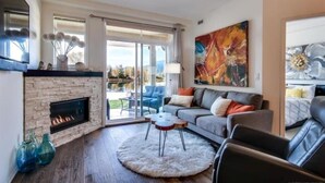 A modern living room with a fireplace, a large sofa, a coffee table, and a painting on the wall. - Tranquil Waterfront Condo (Kelowna)