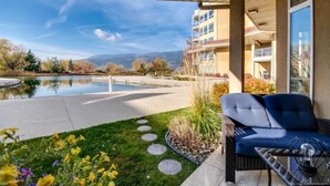 A covered outdoor area with a pool, a grassy area with stepping stones, and a seating area with a table and chairs. - Tranquil Waterfront Condo (Kelowna)