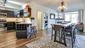A modern kitchen with dark cabinetry, a central island, and a dining area with bar stools. - Tranquil Waterfront Condo (Kelowna)