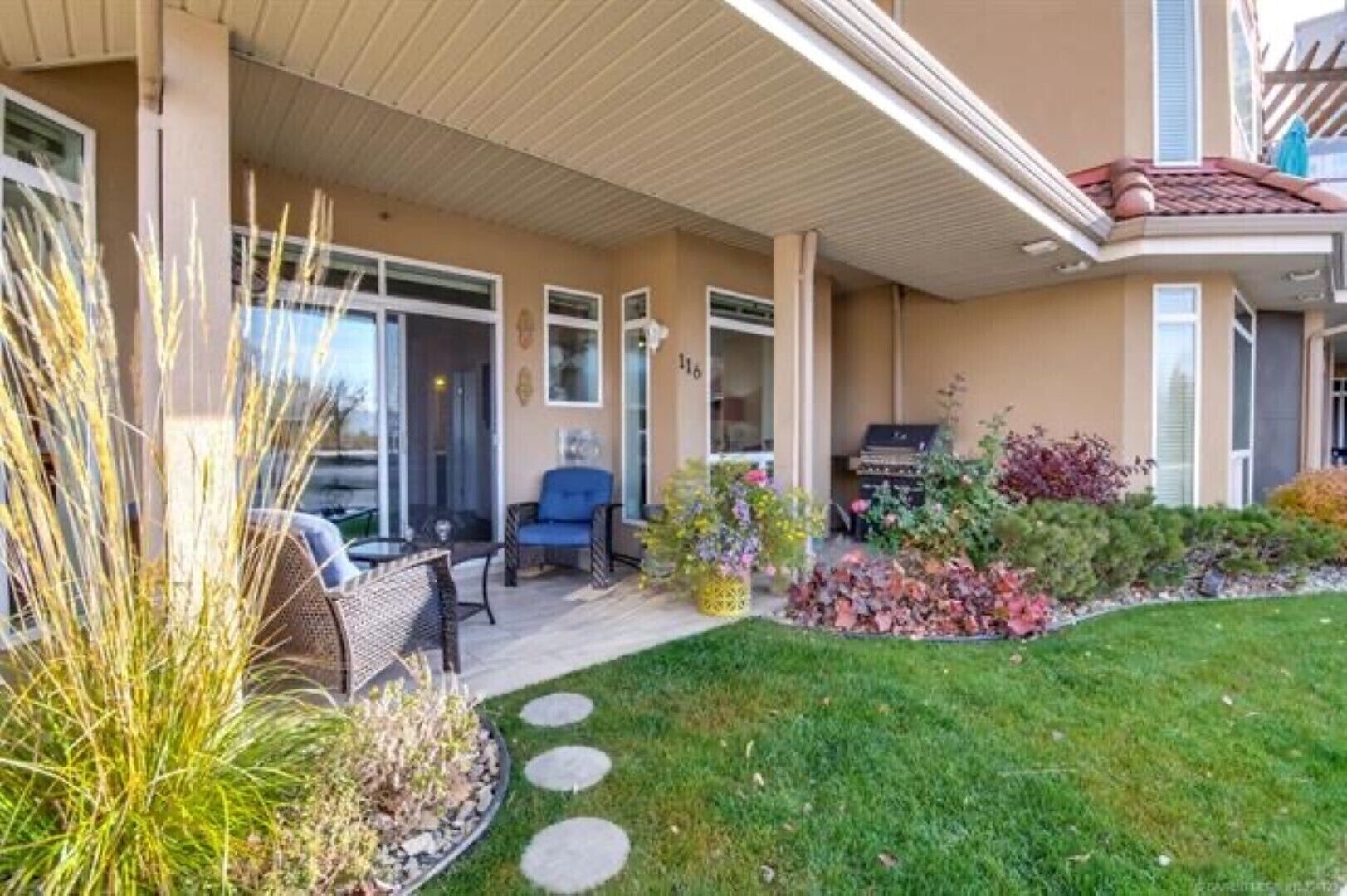 A covered patio with outdoor seating, a barbecue grill, and a well-maintained garden with various plants and stepping stones.