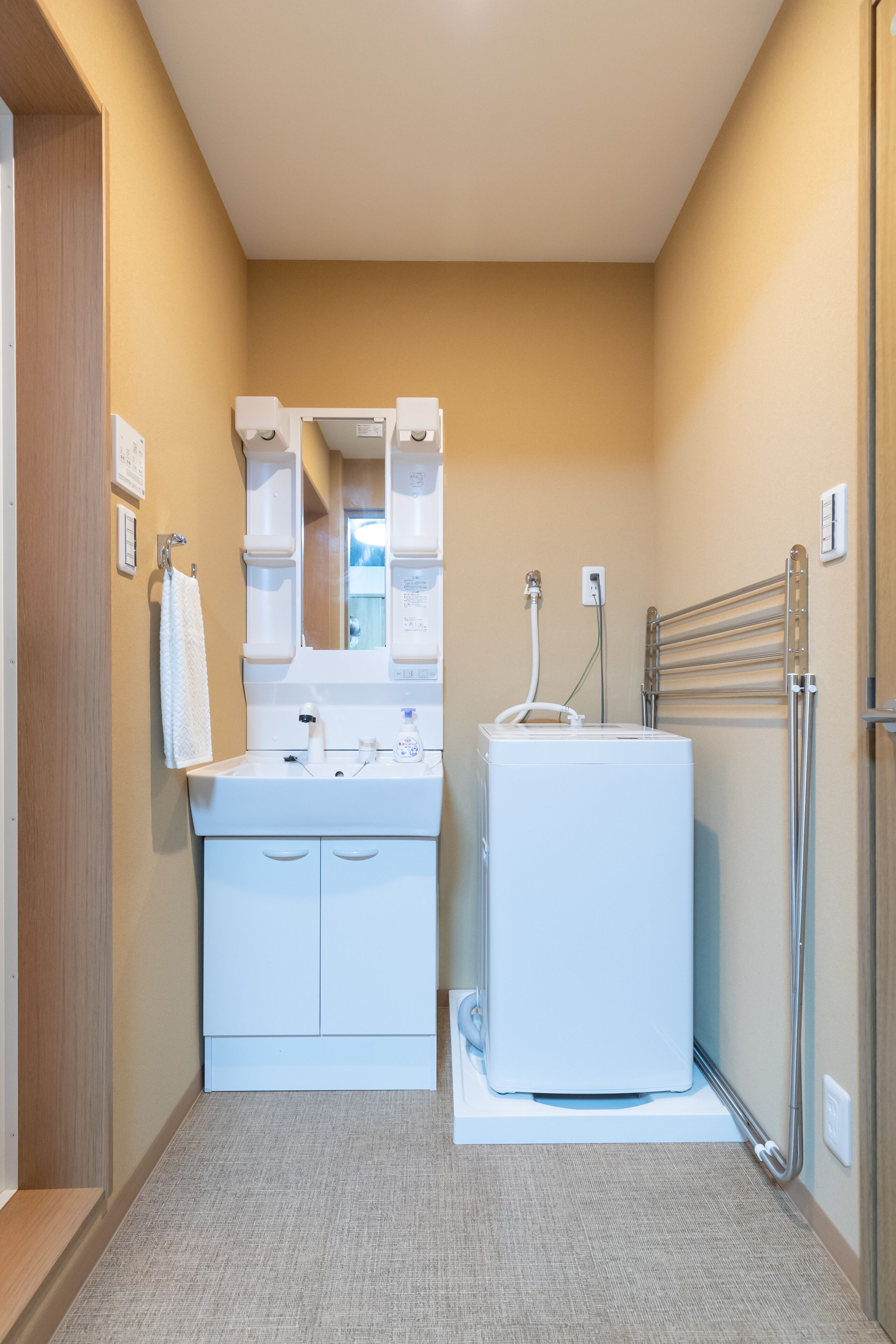 A small bathroom with a white sink, mirror, and towel rack. There is a white heater and a towel hanging on the wall.