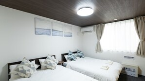 Habitación de hotel con dos camas, una lámpara en el techo, una ventana con cortinas y un aire acondicionado instalado en la pared.