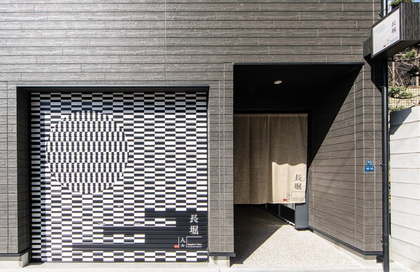 Un edificio moderno con un estampado de cuadros en la puerta del garaje, una entrada despejada y un letrero con caracteres japoneses.