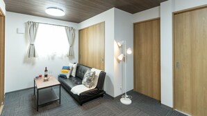 Una habitación moderna con un sofá, una mesita con una botella y vasos, una lámpara de pie y puertas de madera.