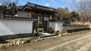 Una casa japonesa tradicional con tejado de tejas, pared de piedra y un pequeño jardín con plantas en macetas.