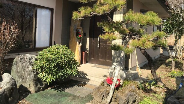 Una casa tradicional japonesa con un jardín bien cuidado, que incluye un bonsái y un farol de piedra.