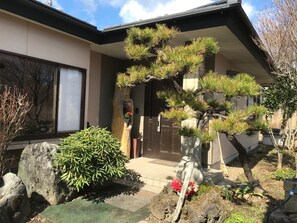 Una casa tradicional japonesa con un jardín bien cuidado, que incluye un bonsái y un farol de piedra.
