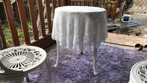 Una mesa redonda con mantel blanco, un tapete morado y una valla de madera al fondo.