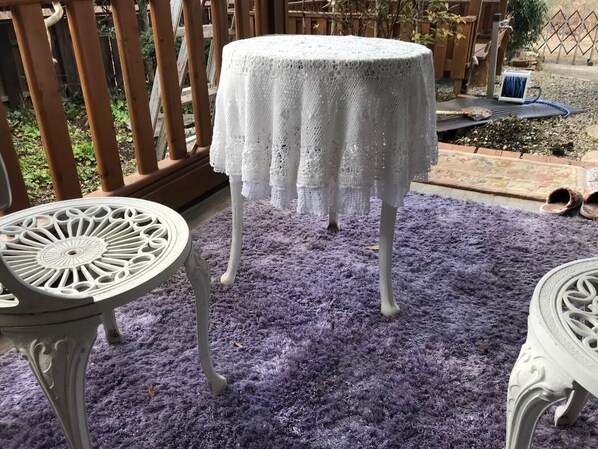 Una mesa redonda con mantel blanco, un tapete morado y una valla de madera al fondo.