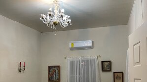 Uma sala de estar com um candelabro, um conjunto de sofás, uma poltrona e uma janela grande com cortinas.