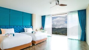 Habitación de hotel con dos camas, un ventanal con vistas a las montañas y una pared de acento azul.