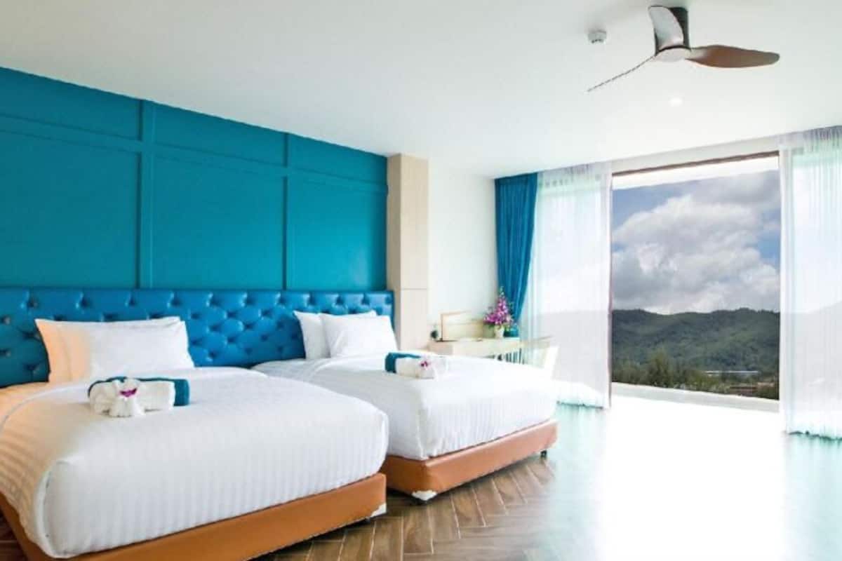 Une chambre d’hôtel avec deux lits, une grande fenêtre donnant sur les montagnes et un mur d’accent bleu.