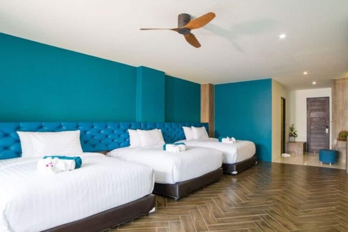 Une chambre d’hôtel avec trois lits, un ventilateur de plafond et un plancher en bois.