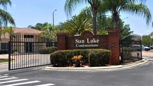 A gated entrance with a sign for Sun Lake Condominiums, surrounded by palm trees and a clear sky.