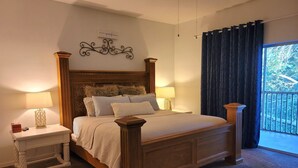 A neatly made bed with a wooden headboard, two bedside tables with lamps, a decorative wall piece, and a view through a window with curtains.