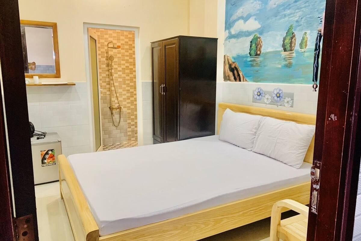 A bedroom with a bed, a wardrobe, a shower area, and a painting of a coastal scene.