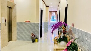 Un pasillo de hotel con piso de baldosas, un mostrador de recepción con sillas y un letrero que indica el área de ascensores.