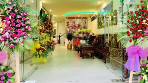 Un vestíbulo de hotel con una escalera central, arreglos florales y mobiliario de madera.