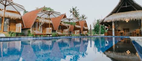 A pool area with thatched-roof bungalows and umbrellas.