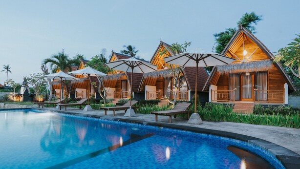 Un resort con cabañas de techo de paja, piscina y zonas de estar al aire libre.