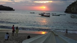 Escena de playa con barcos en el agua y gente en la orilla.