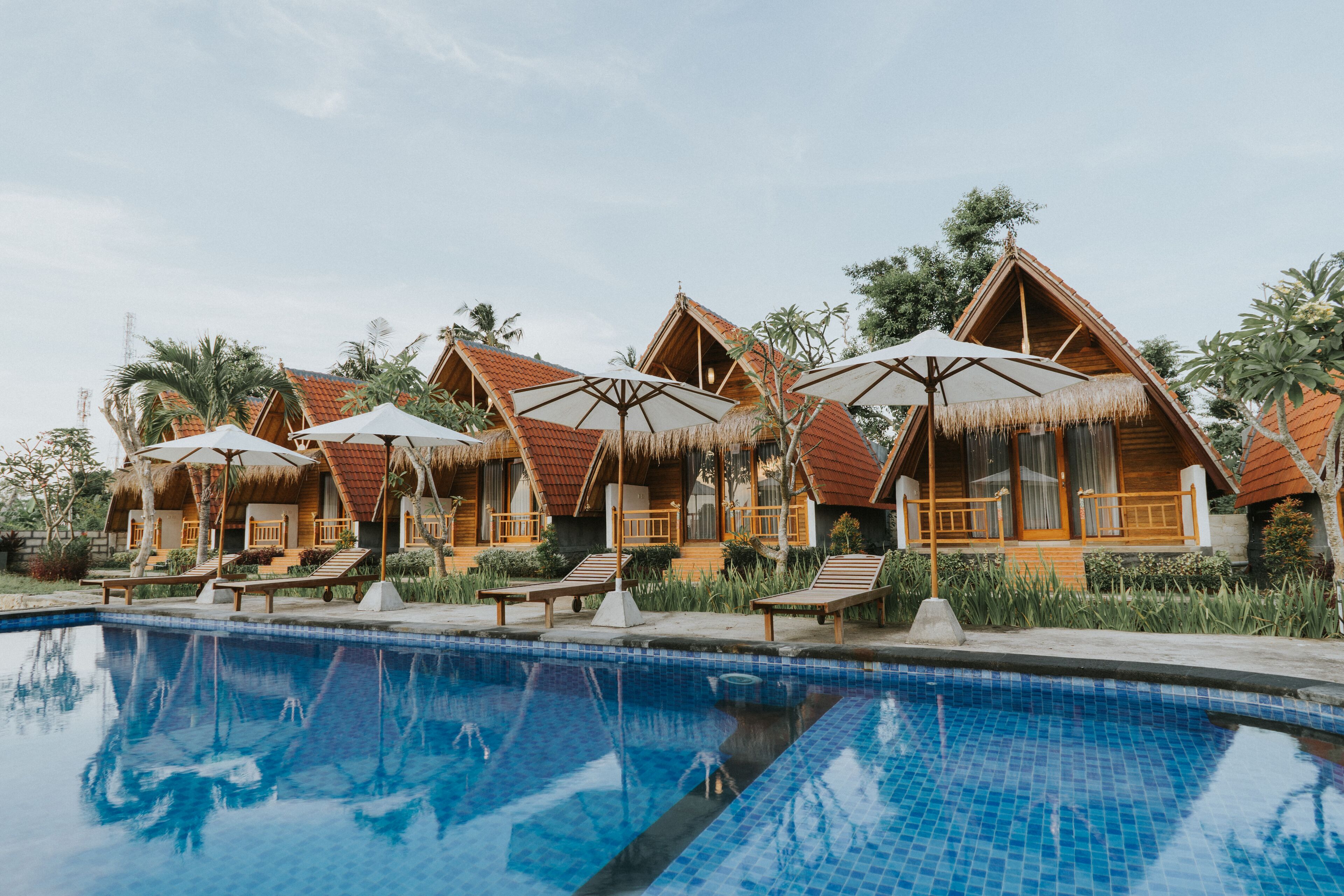 Un espace aménagé au bord de la piscine, avec des bungalows aux toits de chaume et des chaises longues.