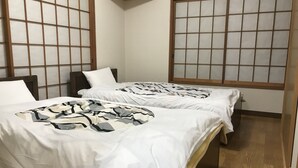 A hotel room with two beds, each with a white bedspread and a patterned blanket. The room has wooden flooring and a traditional Japanese-style window with a grid pattern. - Nasukogen Holiday (Nasu)