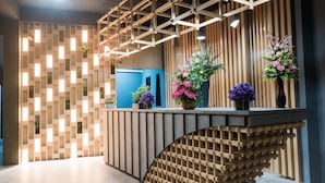 A reception desk with a modern design, featuring a wooden slat wall and a curved wooden structure beneath it. - Little Loft Hotel (Wichit)