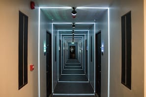 A long, narrow hallway with a modern design, featuring a series of doors on either side and a central light strip running down the middle.