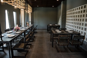 Un restaurante con mesas y sillas largas, piso de baldosas y una pared decorativa con recortes cuadrados.