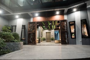 A modern lobby with a central elevator, potted plants, and a stone wall.
