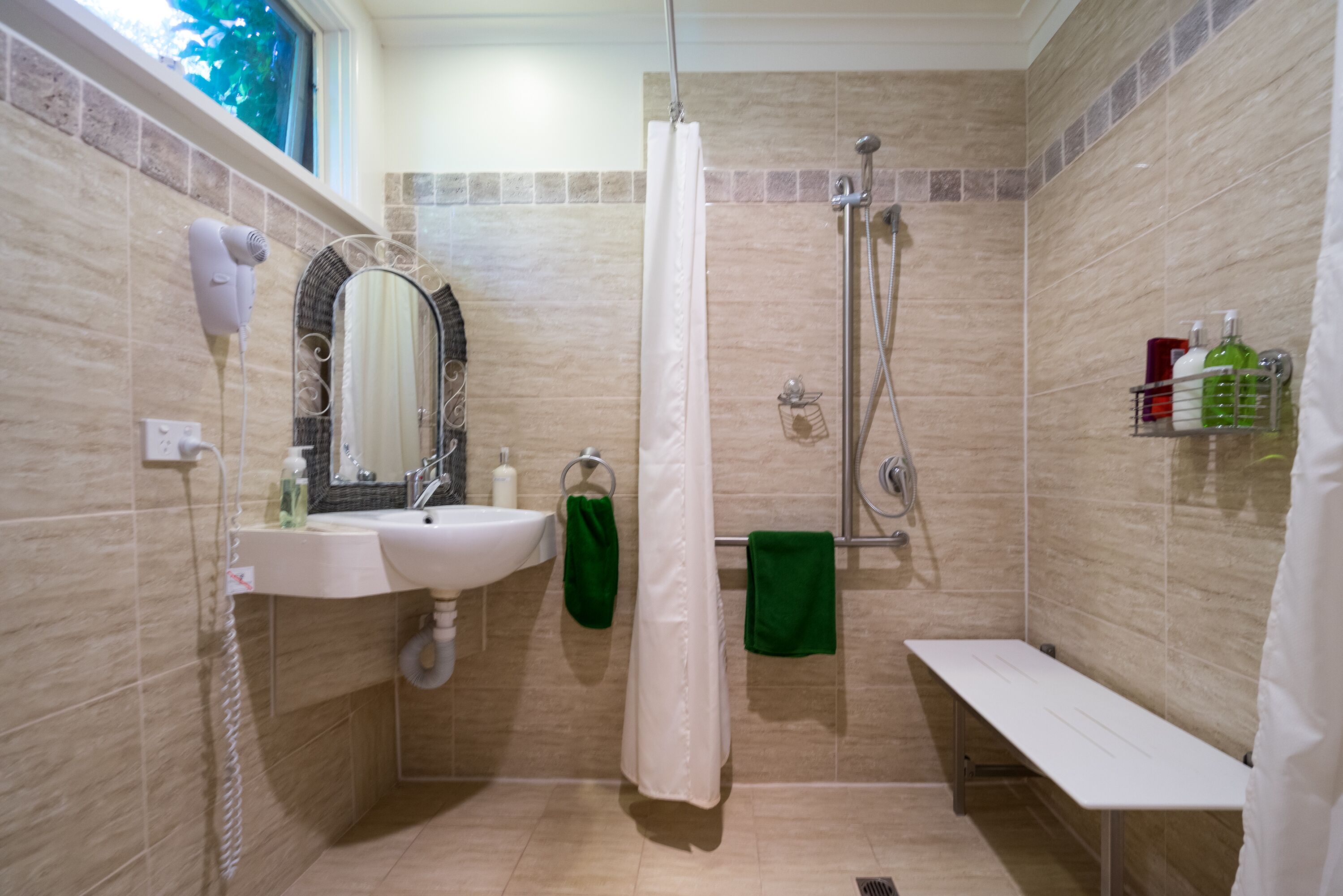 Un baño con ducha, lavamanos, espejo y toallero.