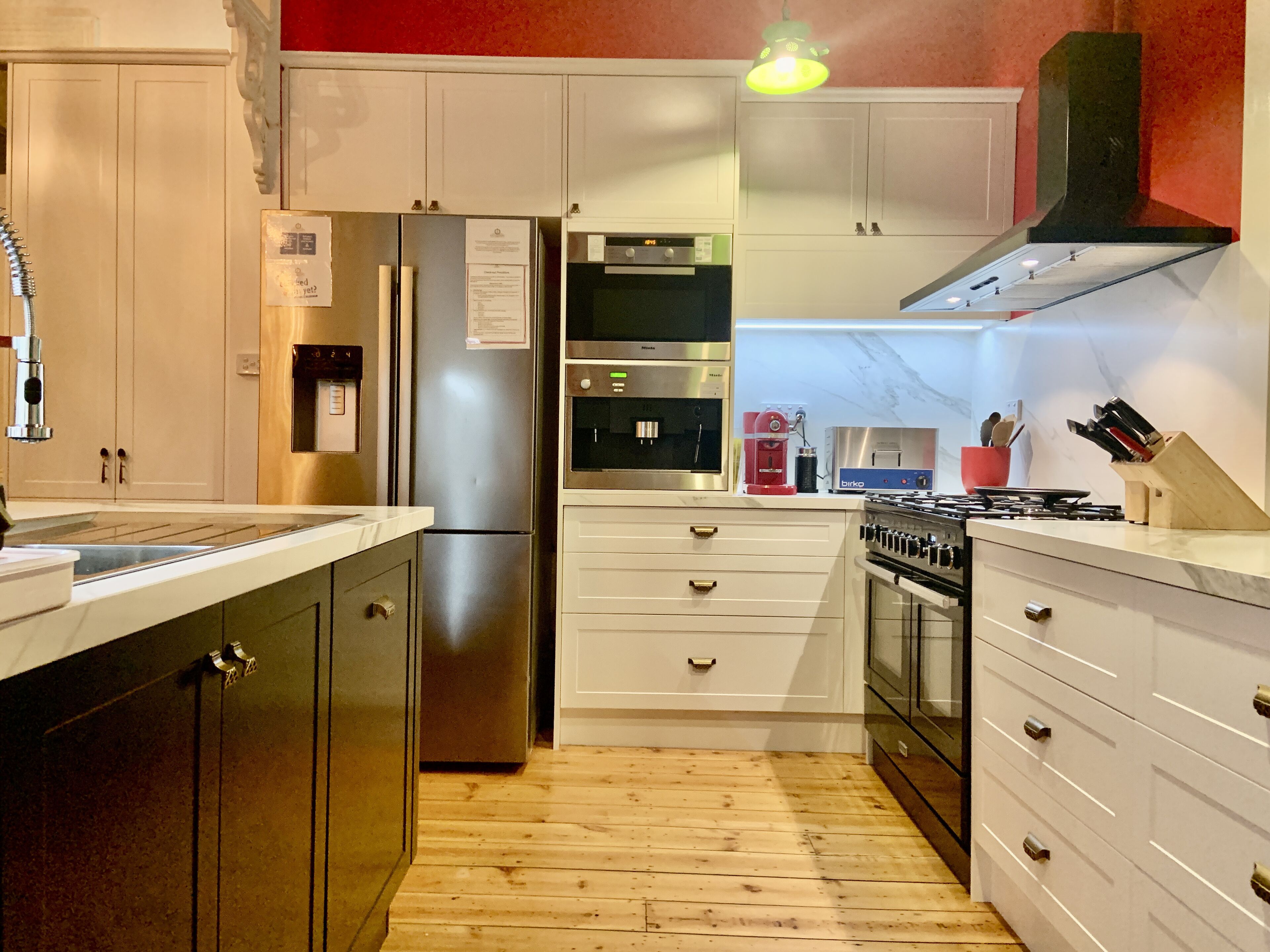 A modern kitchen with stainless steel appliances, white cabinetry, and a wooden floor.