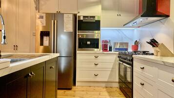 A modern kitchen with stainless steel appliances, white cabinetry, and a wooden floor.