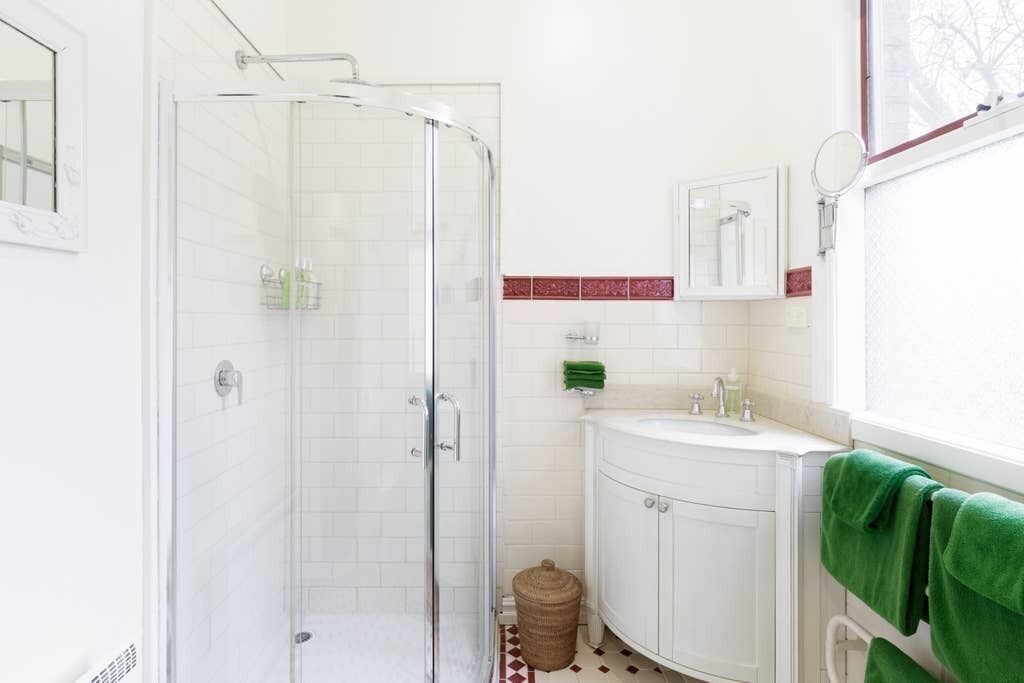 A bathroom with a glass-enclosed shower, white tiled walls, a white sink, and a mirror above it.