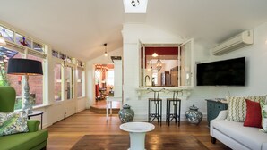 A spacious living area with a green sofa, white armchair, and a white coffee table. There is a TV mounted on the wall, a fireplace, and a dining area visible through an open doorway. - The Eaglehawk Country House Hotel Maldon (Maldon)