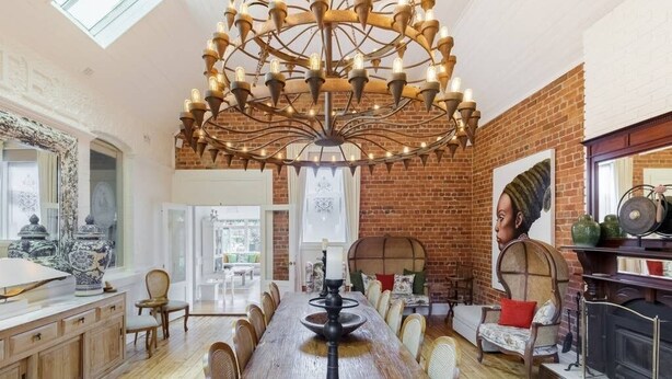 A dining area with a long wooden table, wicker chairs, a chandelier, and a brick wall. - The Eaglehawk Country House Hotel Maldon (Maldon)